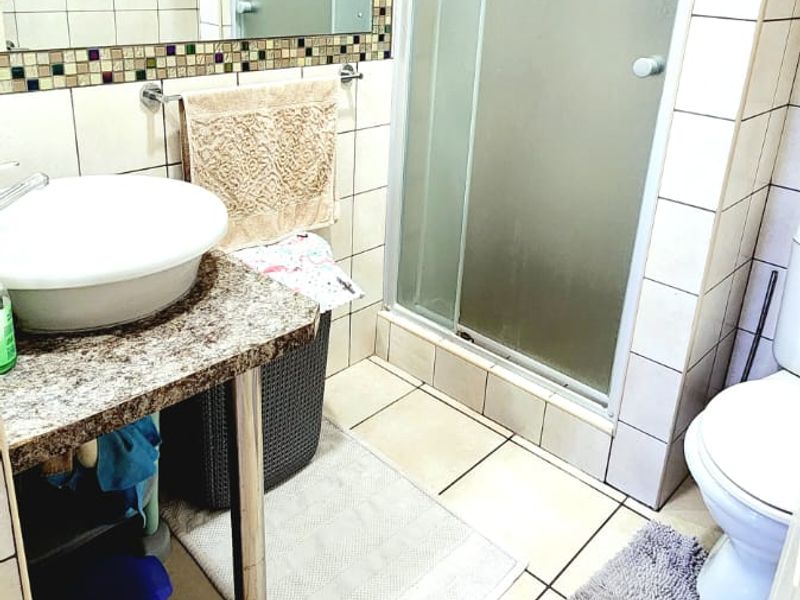 A functional bathroom featuring a vessel sink on a granite vanity, a glass shower enclosure, and neutral wall and floor tiling.