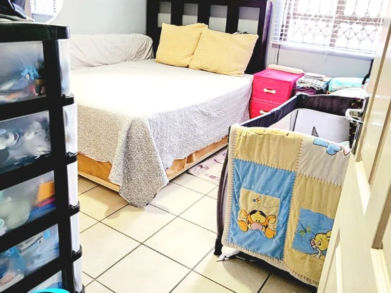 A functional bedroom featuring tiled flooring, a wall-mounted air conditioning unit, and a window fitted with security bars and venetian blinds.