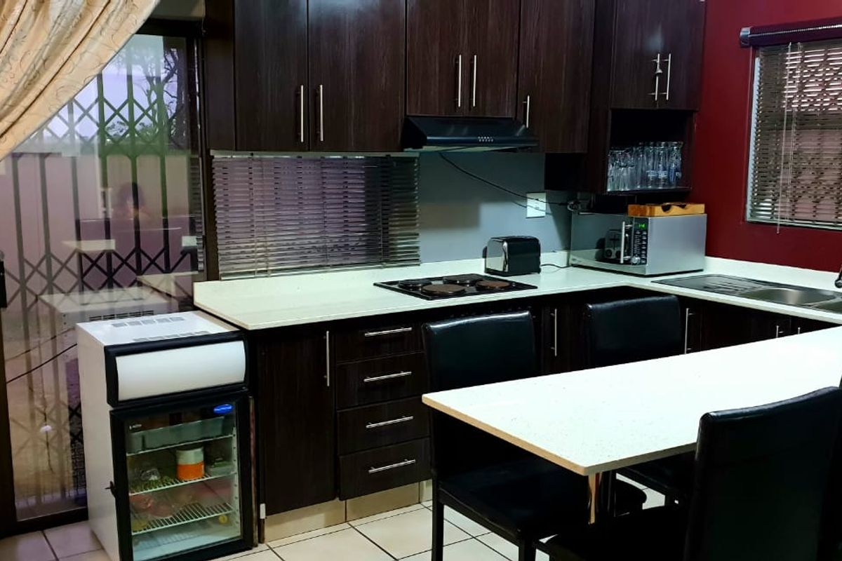 A functional kitchen featuring dark wood cabinetry, a breakfast bar, integrated hob, extractor fan, and a double sink with tiled flooring.