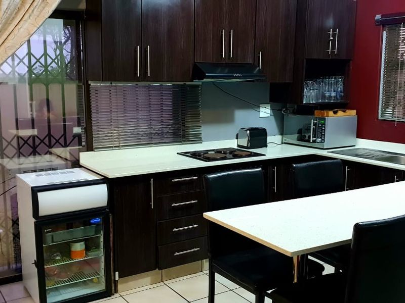 A functional kitchen featuring dark wood cabinetry, a breakfast bar, integrated hob, extractor fan, and a double sink with tiled flooring.
