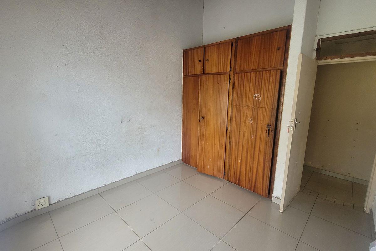 An empty bedroom featuring tiled flooring and built-in wooden cupboards, offering a blank canvas for renovation or interior design updates.