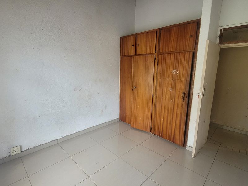 An empty bedroom featuring tiled flooring and built-in wooden cupboards, offering a blank canvas for renovation or interior design updates.