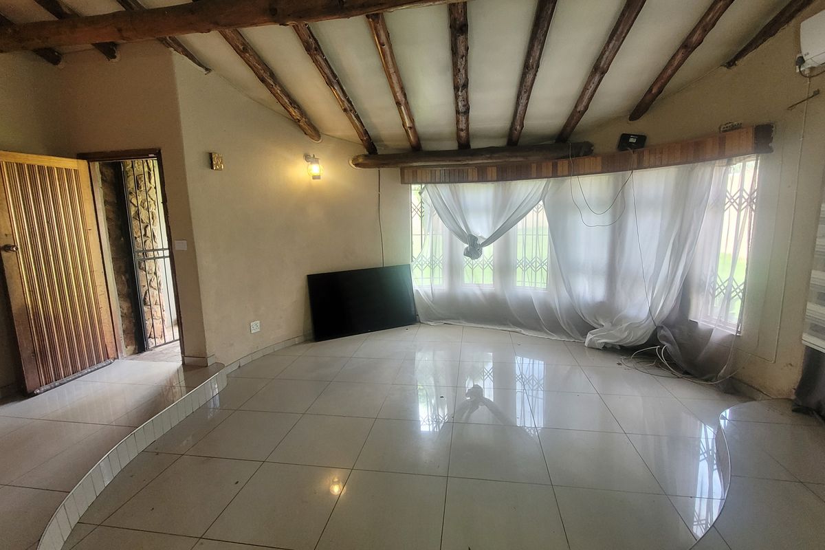 Spacious living area featuring exposed timber ceiling beams, large bay windows with security gates, tiled flooring, and an integrated air conditioning unit.