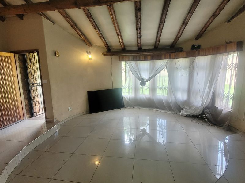 Spacious living area featuring exposed timber ceiling beams, large bay windows with security gates, tiled flooring, and an integrated air conditioning unit.