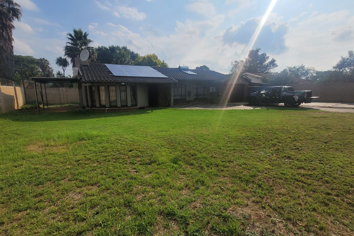 Rear view of the property featuring a large lawn, paved driveway, and solar panels installed on the tiled roof.