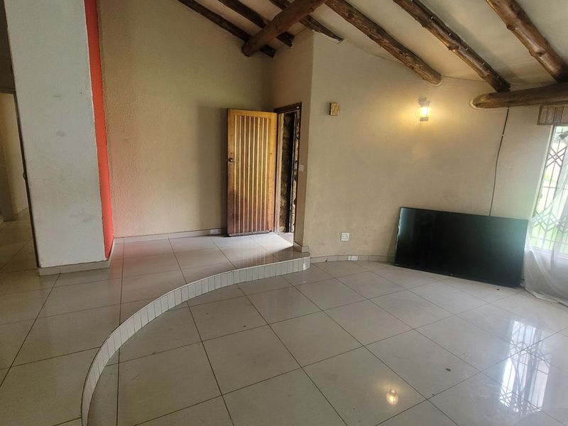 Spacious living area featuring exposed timber ceiling beams, tiled flooring with a raised platform section, and neutral wall finishes.