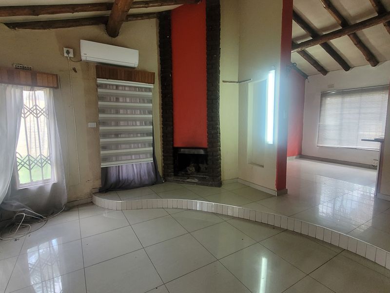 Spacious living area featuring a raised platform, built-in fireplace, exposed timber beams, and tiled flooring, offering a versatile layout for modern living.