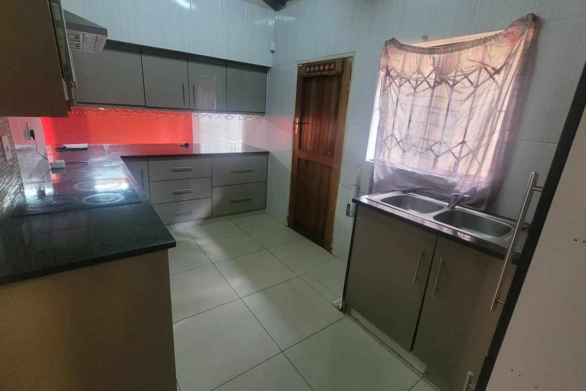 A functional kitchen featuring built-in cabinetry, granite countertops, a double basin sink, and tiled finishes throughout.