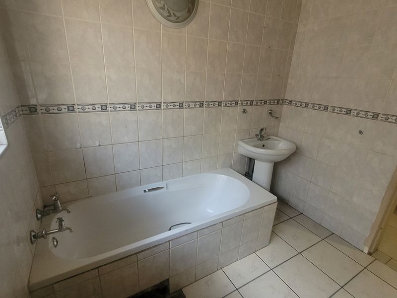 A dated bathroom featuring a built-in bathtub, pedestal washbasin, and full-height ceramic wall tiling, requiring cosmetic updates to modernize the space.