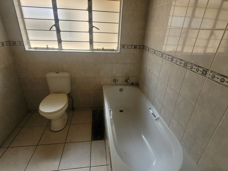 A dated bathroom featuring a built-in bathtub, toilet, and neutral wall tiling, offering a blank canvas for modern renovation.