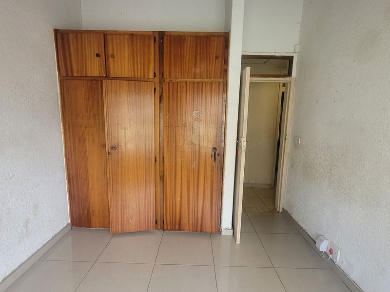 An empty bedroom featuring built-in wooden cupboards and tiled flooring, requiring cosmetic updates to the walls and cabinetry.