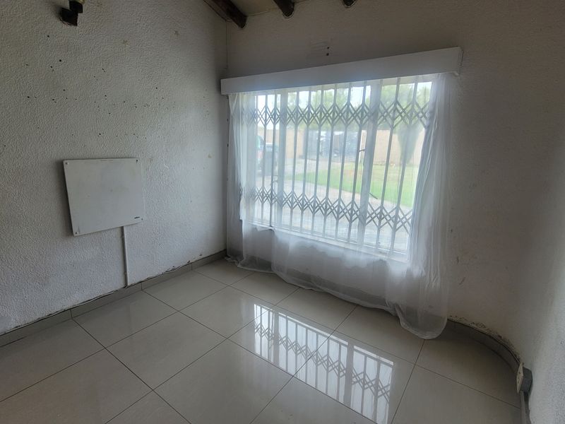 An empty bedroom featuring tiled flooring and a window fitted with a security gate, requiring cosmetic wall repairs and updates.