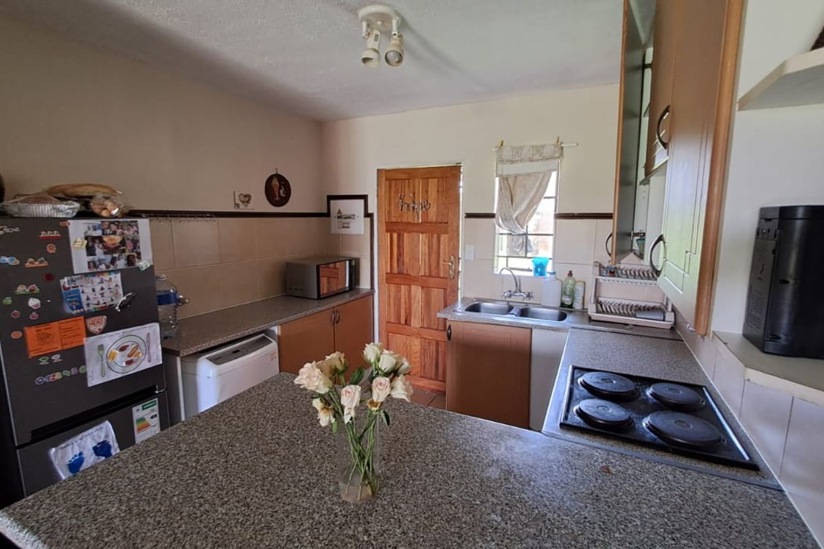 A functional kitchen featuring granite countertops, built-in cabinetry, an electric hob, and a double basin sink with a tiled backsplash.