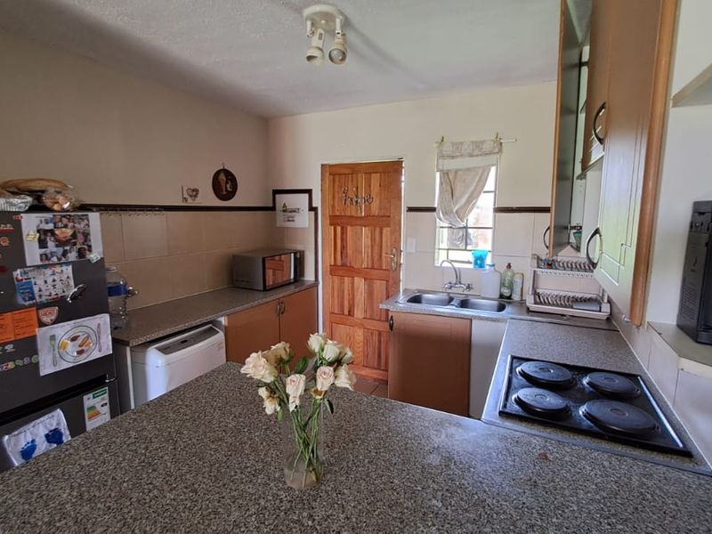 A functional kitchen featuring granite countertops, built-in cabinetry, an electric hob, and a double basin sink with a tiled backsplash.