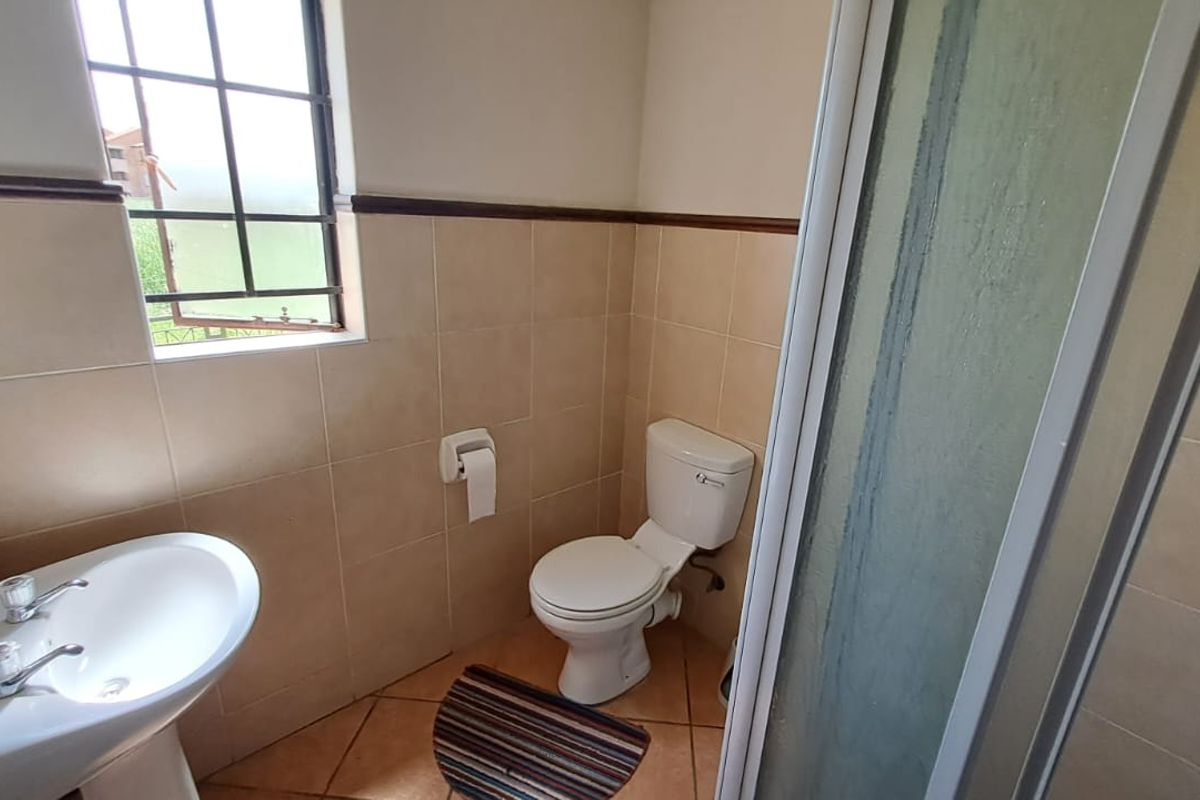 A functional bathroom featuring a pedestal basin, toilet, and shower enclosure with neutral ceramic wall and floor tiling.