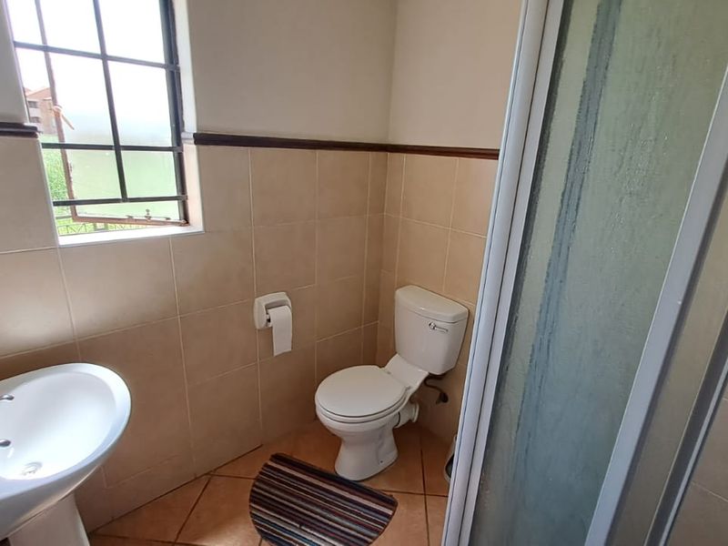 A functional bathroom featuring a pedestal basin, toilet, and shower enclosure with neutral ceramic wall and floor tiling.