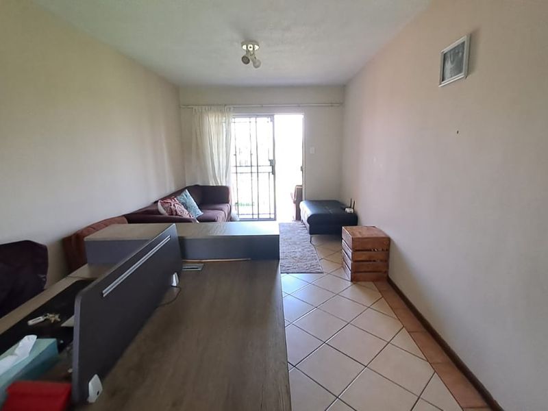 A living room area featuring ceramic floor tiles and a security gate leading to an outdoor space, requiring cosmetic updates to walls and flooring.