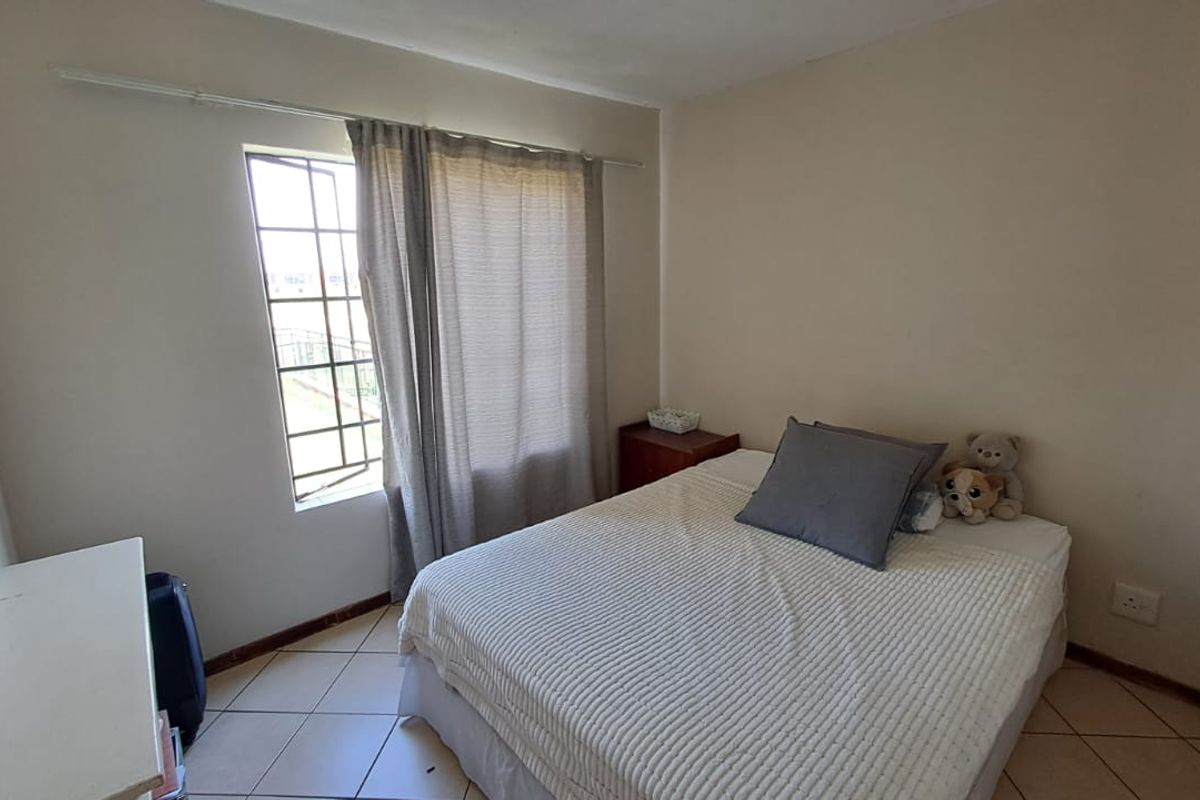 A standard bedroom featuring tiled flooring, a window with security bars, and neutral wall finishes.