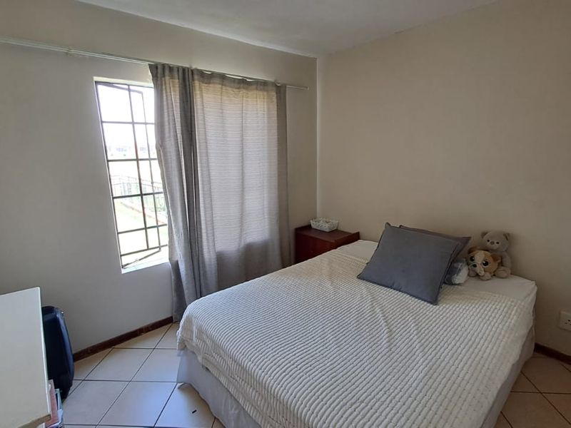 A standard bedroom featuring tiled flooring, a window with security bars, and neutral wall finishes.