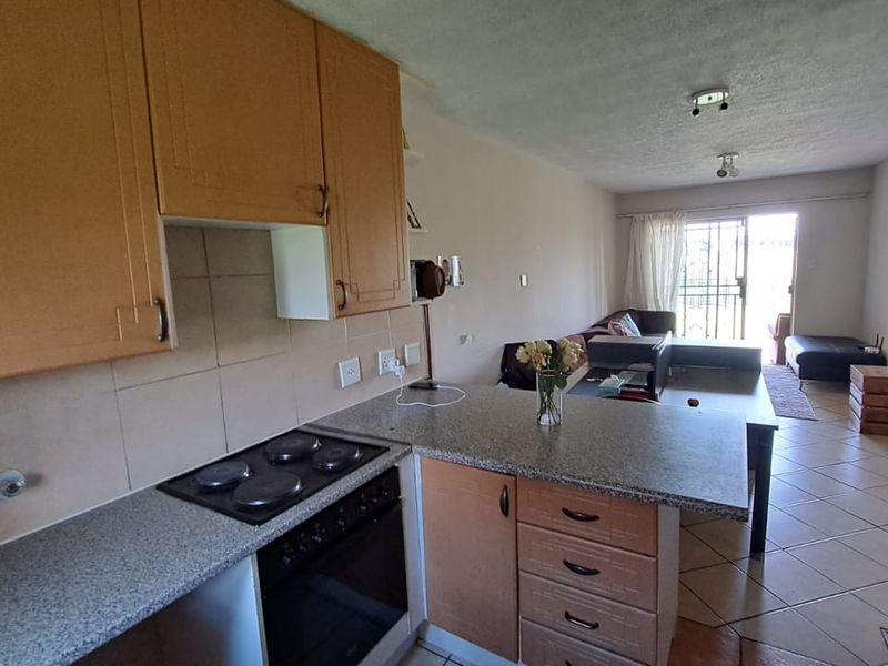 Open-plan kitchen and living area featuring built-in cabinetry, electric cooking appliances, and tiled flooring leading to a balcony with security gate.