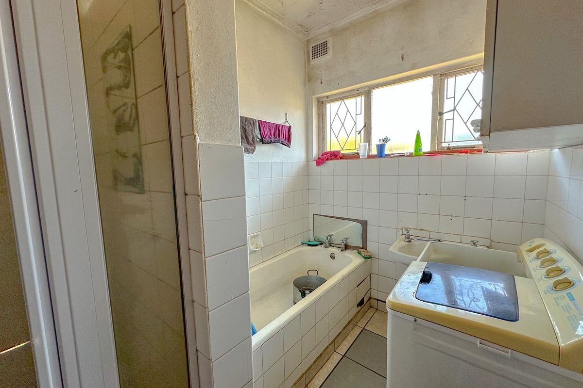 A dated bathroom featuring a built-in bathtub, tiled walls, and a dedicated laundry area with plumbing connections.