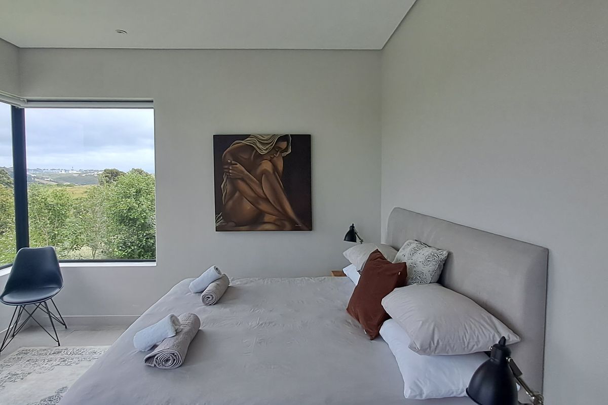 A modern bedroom featuring a large corner window with scenic views, neutral wall finishes, and recessed ceiling lighting.
