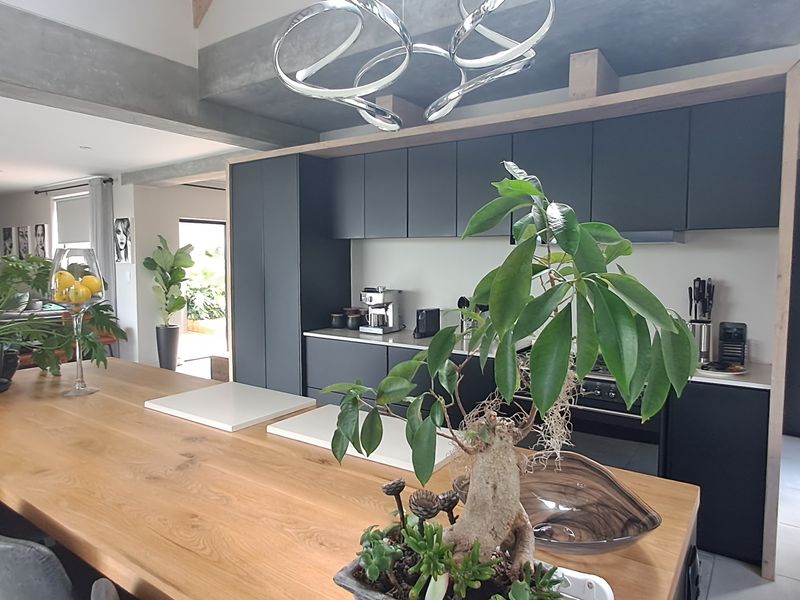 Modern open-plan kitchen featuring a large timber-topped island, sleek dark cabinetry, and exposed concrete architectural beams, seamlessly flowing into the living area.