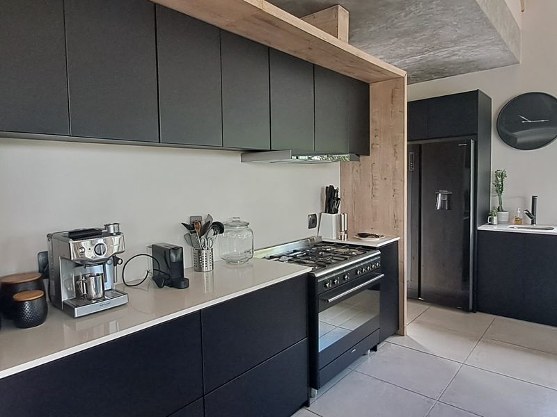 Modern kitchen featuring matte black cabinetry, stone countertops, gas stove, extractor fan, and an exposed concrete ceiling with tiled flooring.