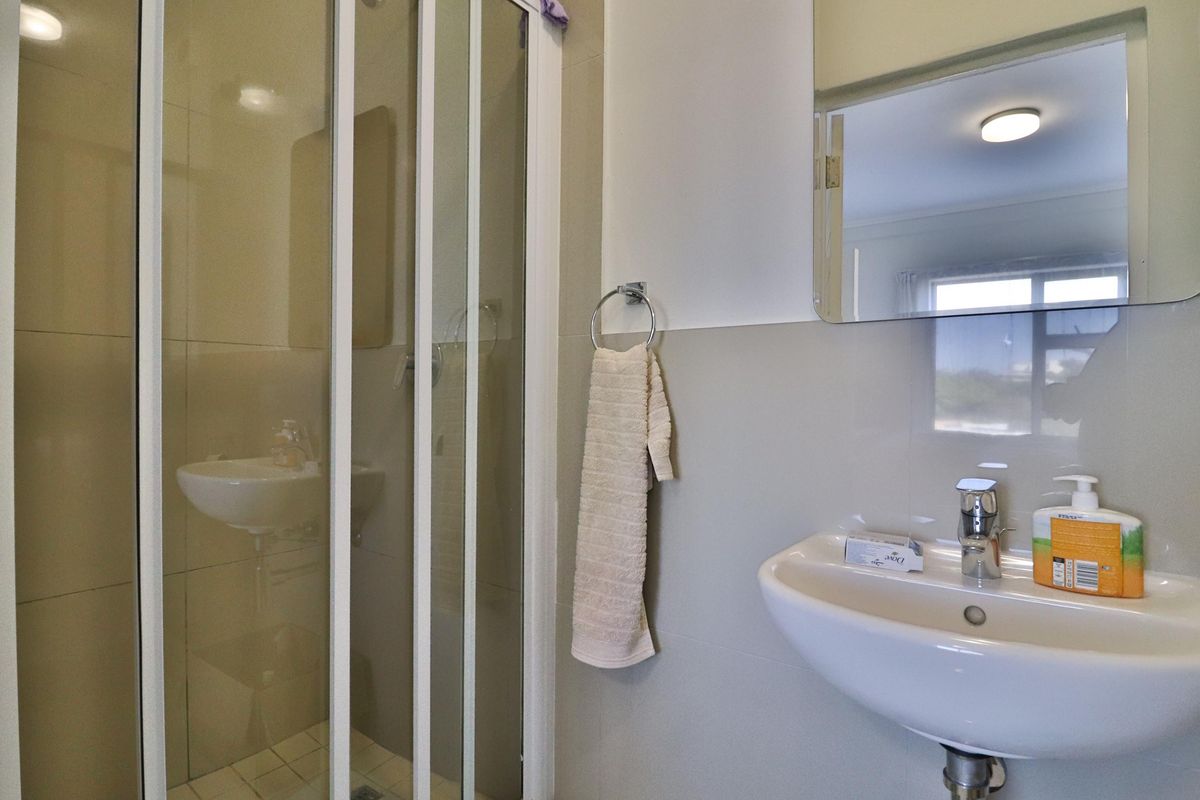 A functional bathroom featuring a wall-mounted basin, a glass-enclosed shower, and a wall-mounted mirror with neutral tiling.