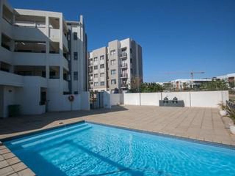 Communal swimming pool area featuring paved decking and modern apartment building architecture in a well-maintained residential complex.