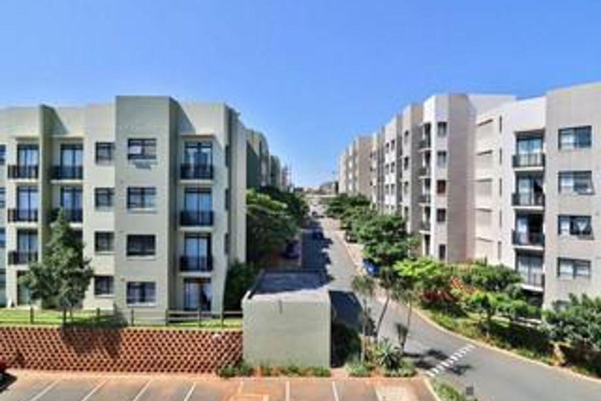 An elevated view of a modern apartment complex featuring multi-story residential buildings, paved parking areas, and landscaped surroundings.