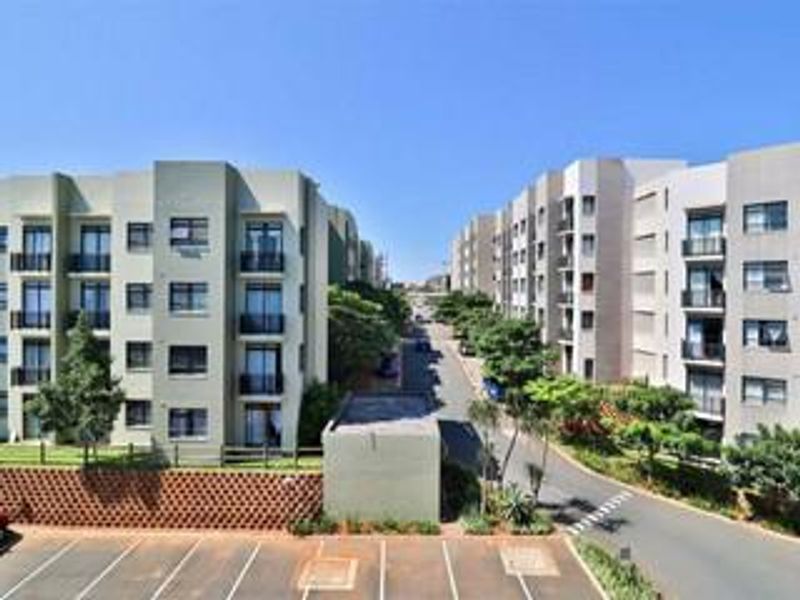 An elevated view of a modern apartment complex featuring multi-story residential buildings, paved parking areas, and landscaped surroundings.