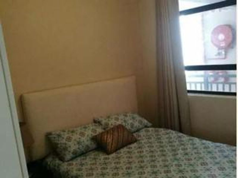 A compact bedroom featuring a neutral color palette, a large window providing natural light, and a built-in headboard.