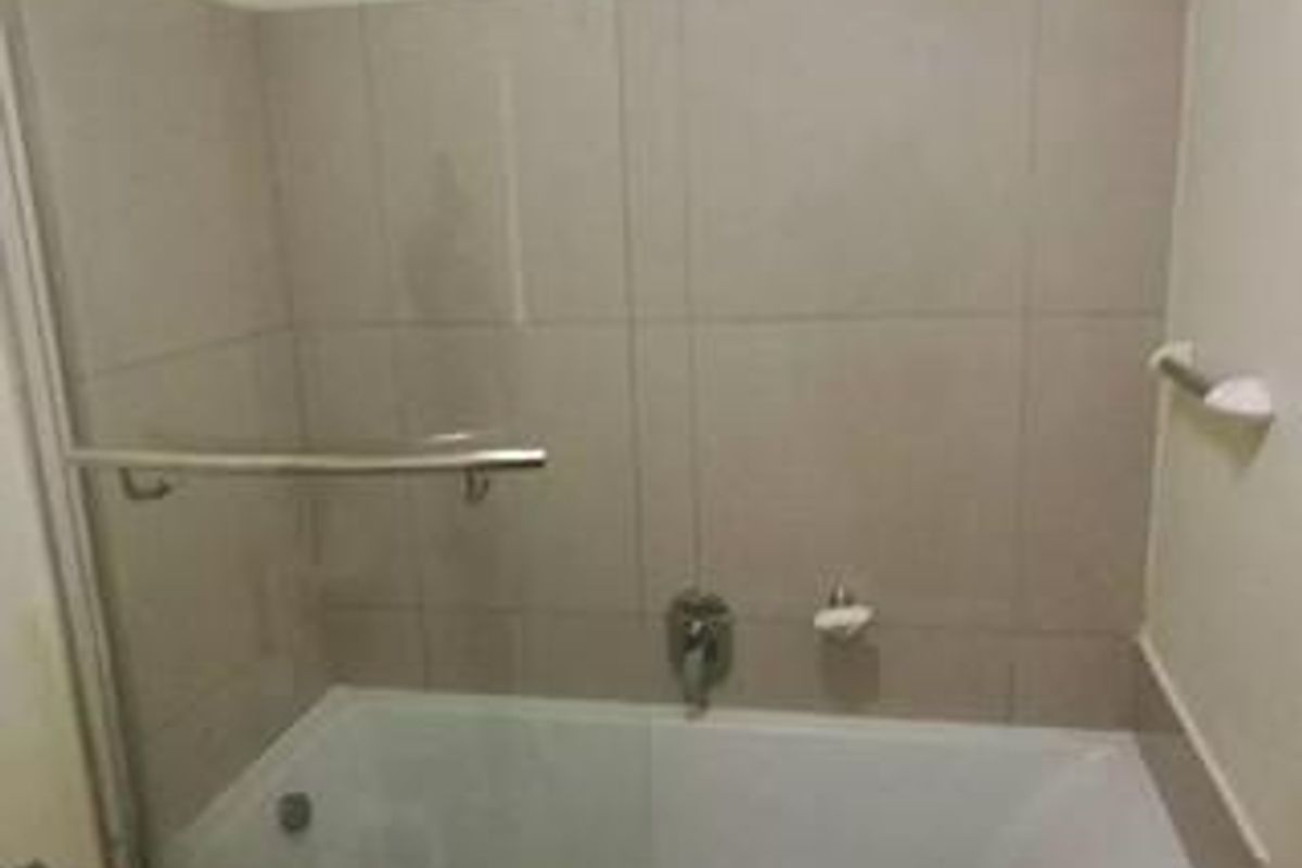 A functional bathroom featuring a built-in bathtub with a glass shower screen, chrome mixer tap, and neutral wall tiling.