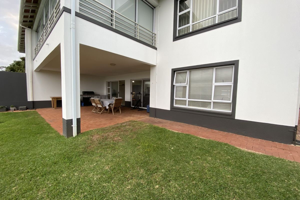 Rear view of the apartment building featuring a covered patio with terracotta paving, a lawn area, and a balcony with metal railings.