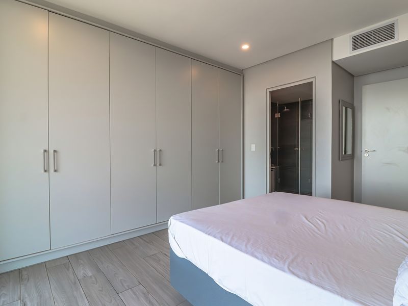 Modern bedroom featuring extensive built-in wardrobes, light wood-look flooring, ducted air conditioning, and direct access to an en-suite bathroom.