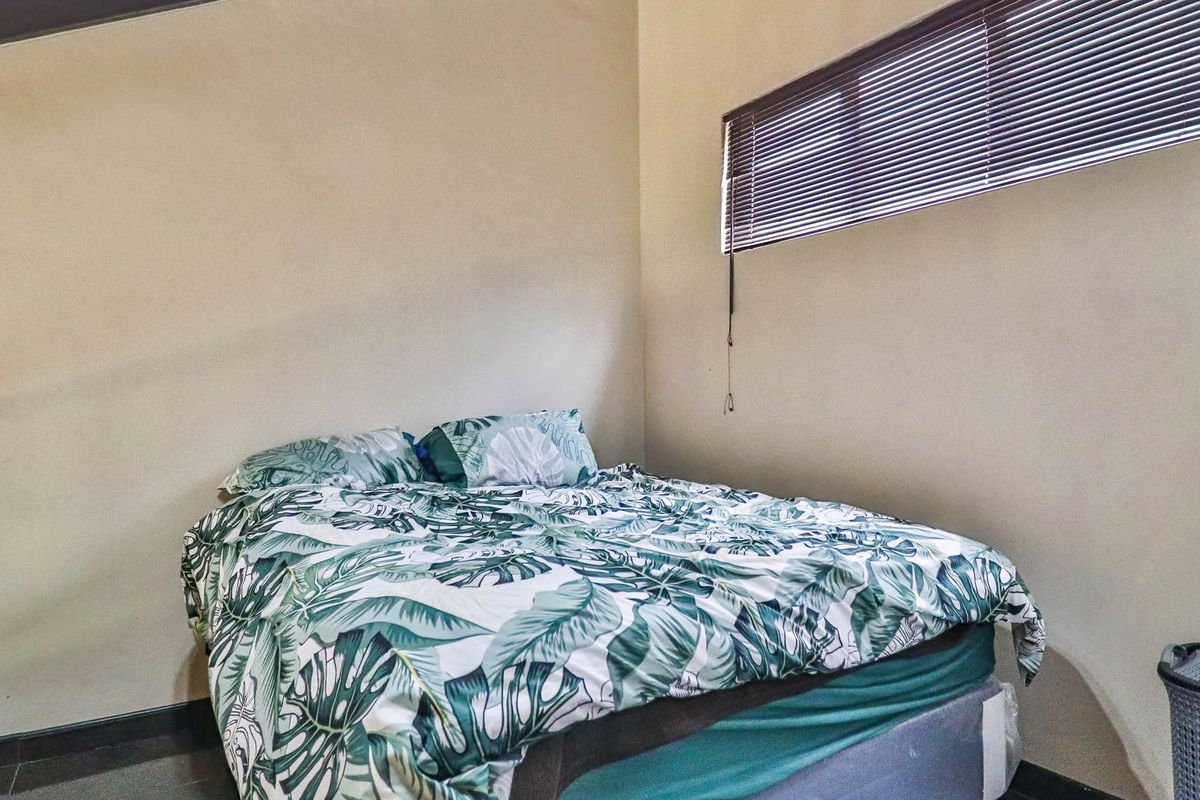 A bedroom featuring neutral walls, dark flooring, and a horizontal window blind.