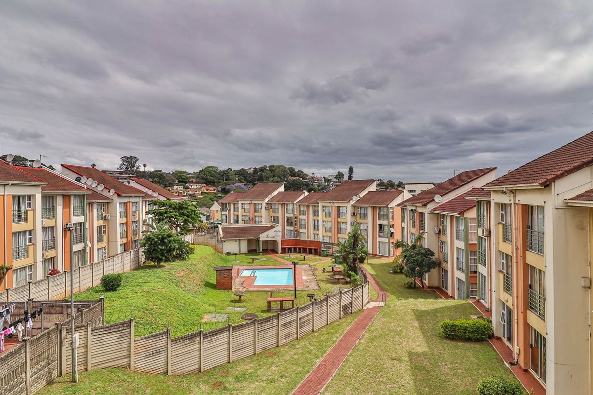 Elevated view of an apartment complex featuring multiple residential blocks, a central communal swimming pool, landscaped garden areas, and paved walkways.
