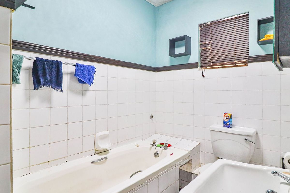 A dated bathroom featuring a built-in bathtub, standard toilet, and wall-mounted basin with tiled splashbacks and a wooden dado rail.
