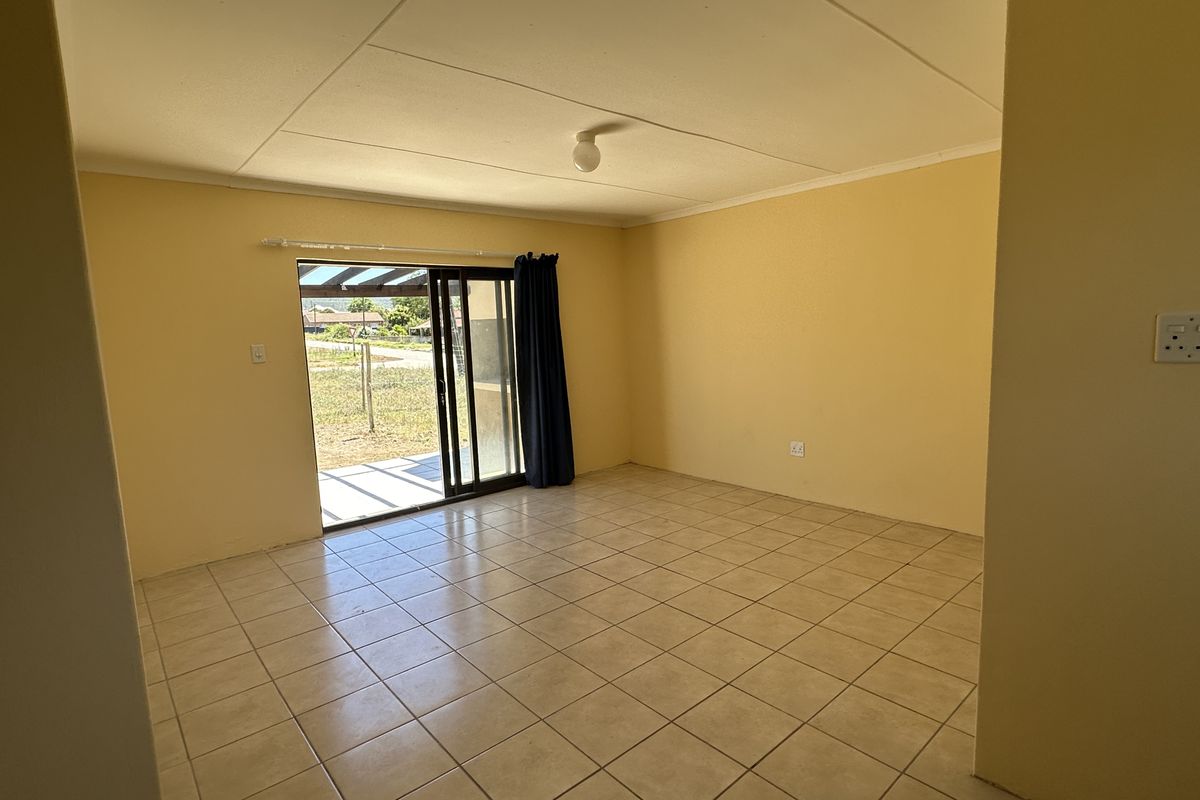 An empty, open-plan living area featuring tiled flooring and a sliding glass door providing direct access to the rear exterior.