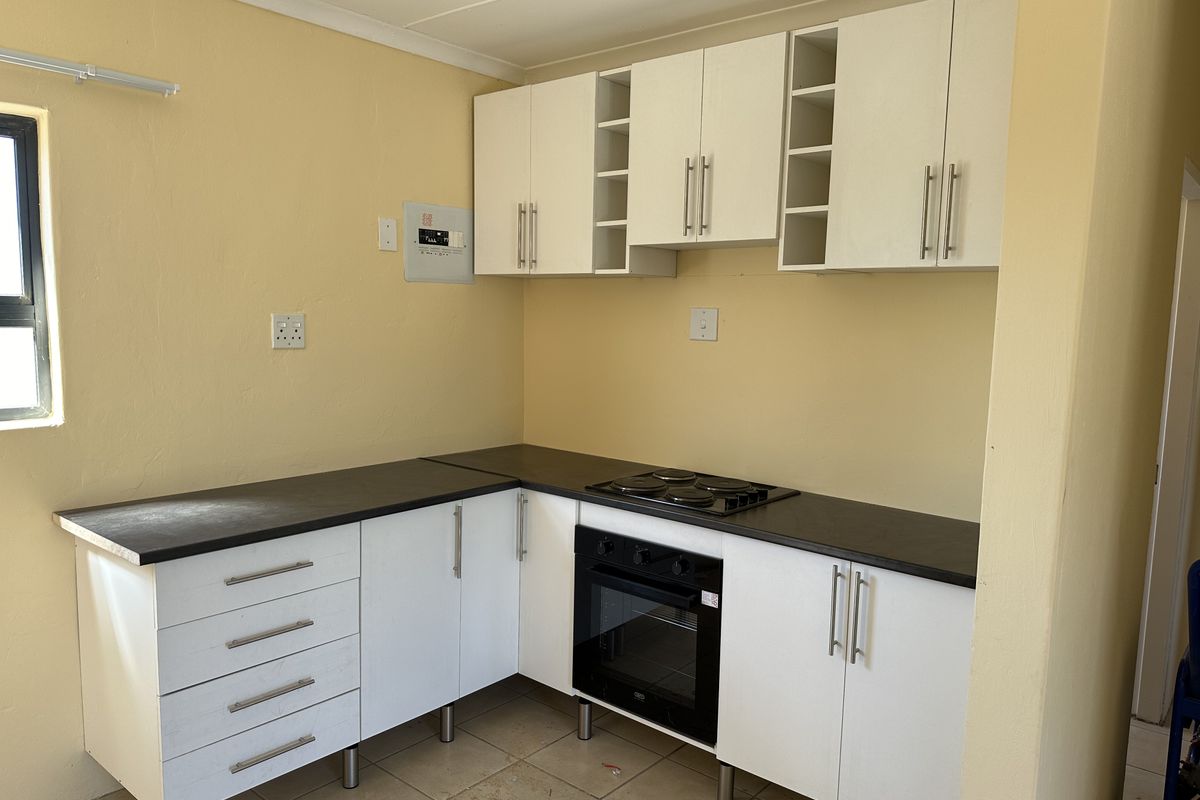 A functional kitchen featuring white cabinetry, dark laminate countertops, a built-in oven, and an electric hob, set against yellow walls with tiled flooring.