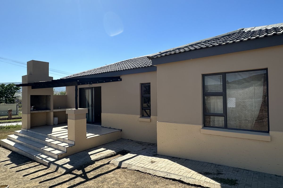 Rear exterior view featuring a tiled patio with a built-in braai, concrete roof tiles, and modern aluminium window frames.