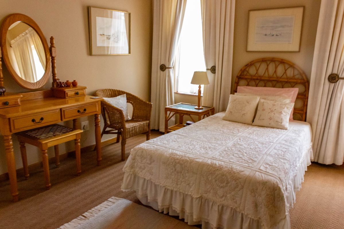 A cozy bedroom featuring neutral wall tones, carpeted flooring, and window treatments, providing a comfortable and functional sleeping space.