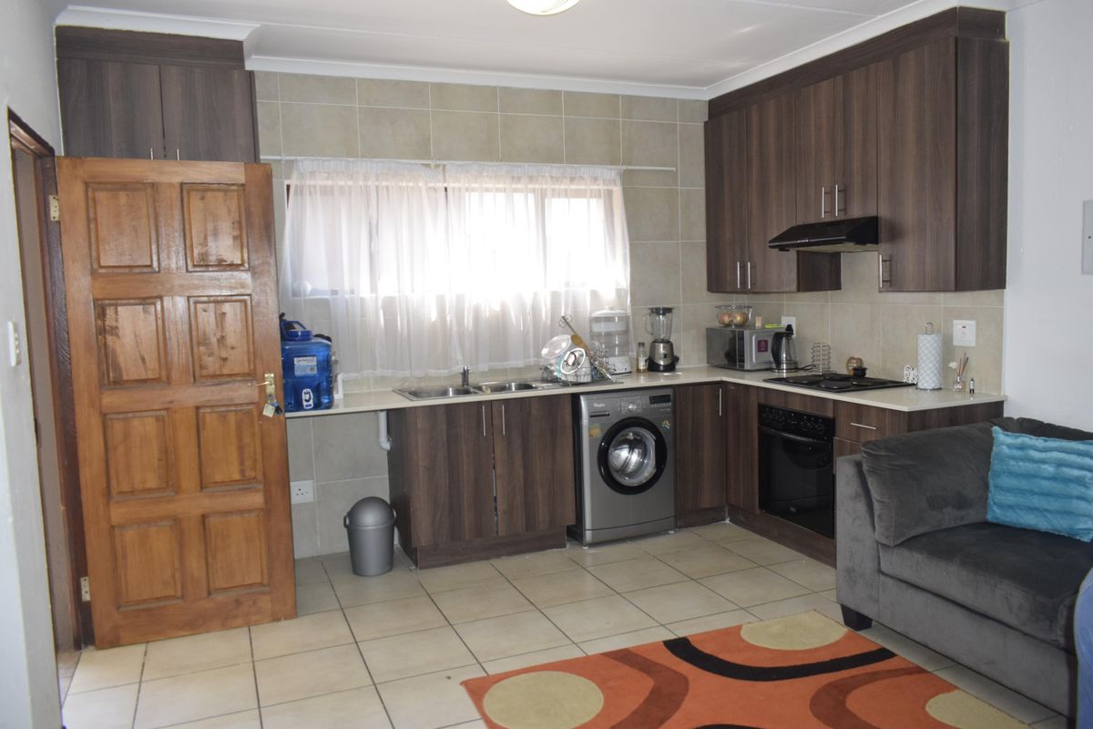 Functional kitchen featuring dark wood-look cabinetry, tiled splashbacks, integrated oven and hob, and tiled flooring with space for laundry appliances.