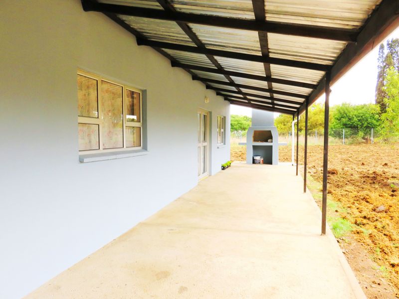 A covered outdoor patio featuring a built-in braai, concrete flooring, and a corrugated metal roof, overlooking an open garden area.