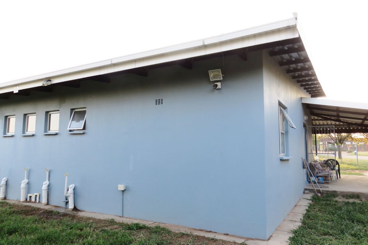 Rear exterior view of the house featuring blue painted walls, security lighting, and a small covered patio area.