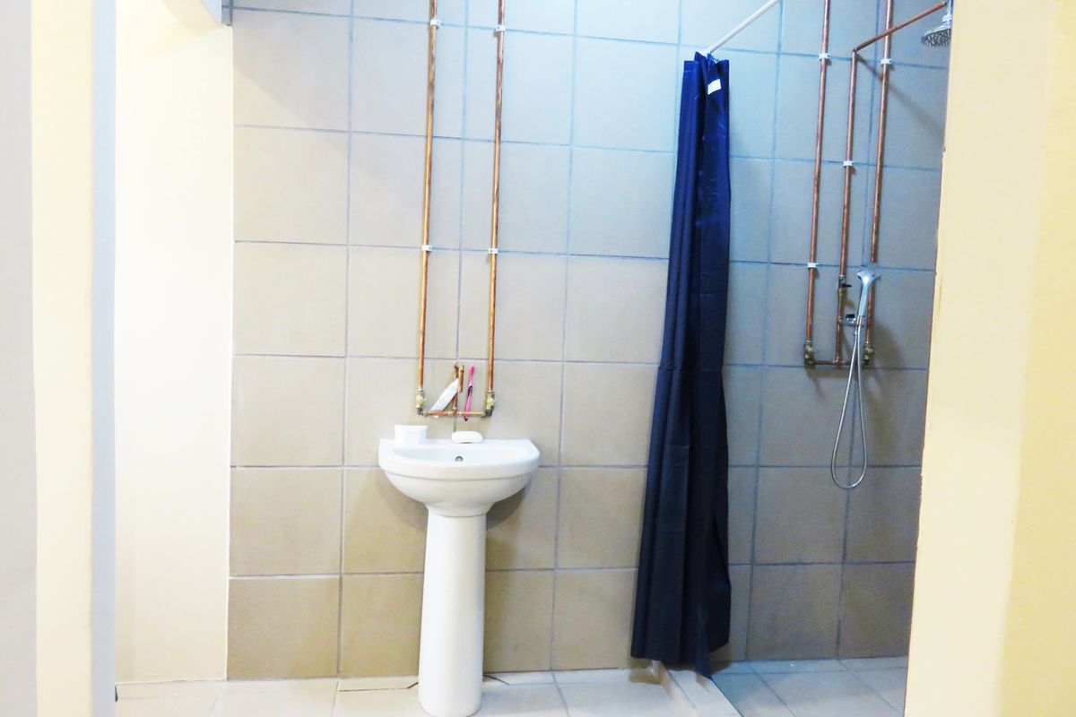A functional bathroom featuring a pedestal basin and shower area with exposed copper plumbing and neutral wall tiling.