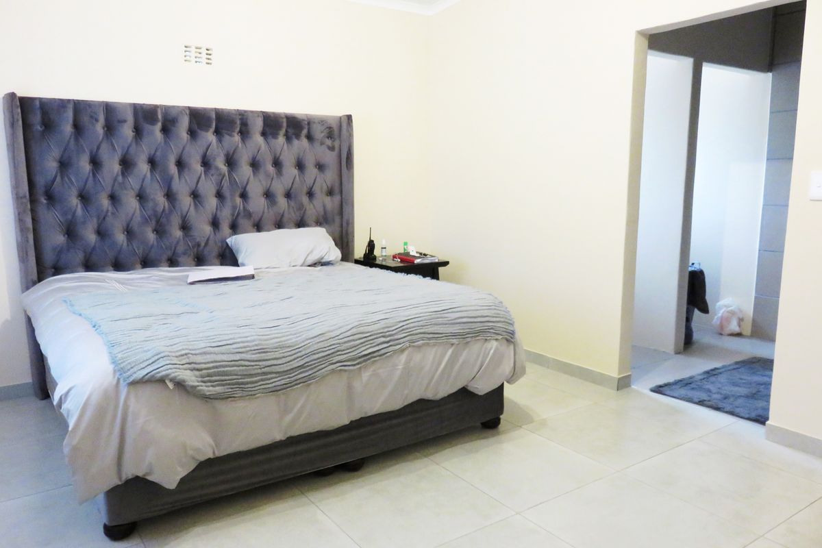 A spacious bedroom featuring neutral tiled flooring and a coved ceiling, with an adjoining doorway leading to an adjacent room.