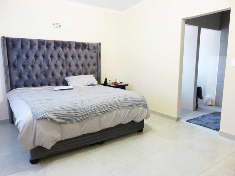 A spacious bedroom featuring neutral tiled flooring and a coved ceiling, with an adjoining doorway leading to an adjacent room.