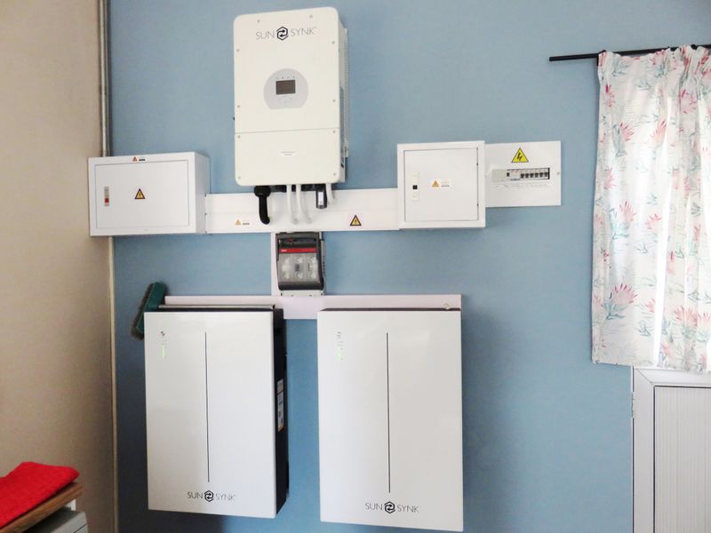 A clean installation of a Sunsynk solar inverter and dual battery storage system mounted on a wall with integrated electrical distribution boards.